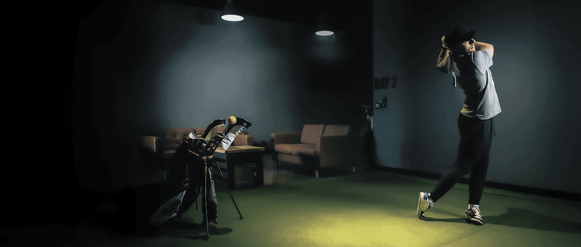 A golfer mid-swing in a Back Nine simulator bay